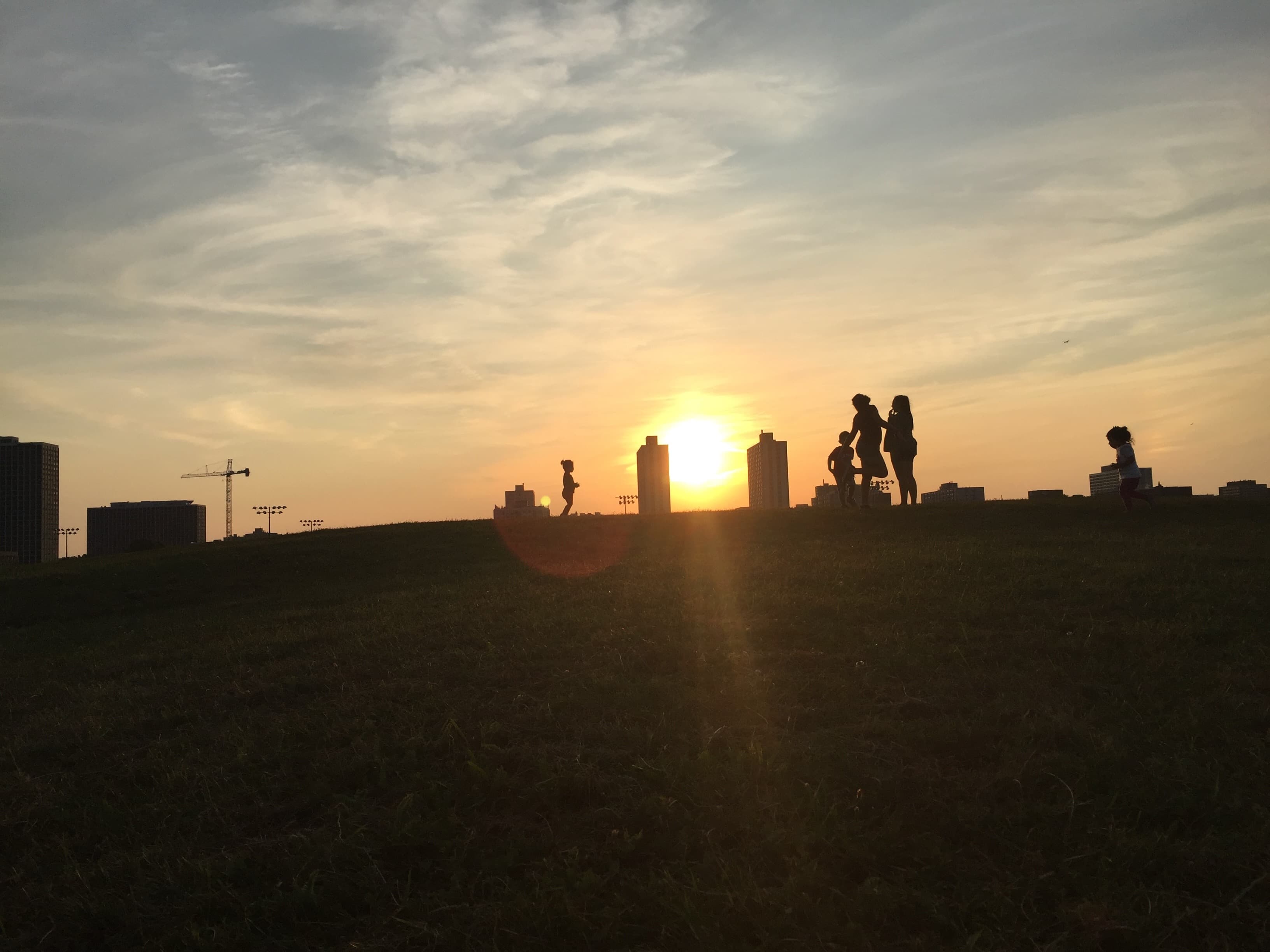 Sunset Silhouettes, City's Edge - Silhouetted figures of a family playing at sunset,...